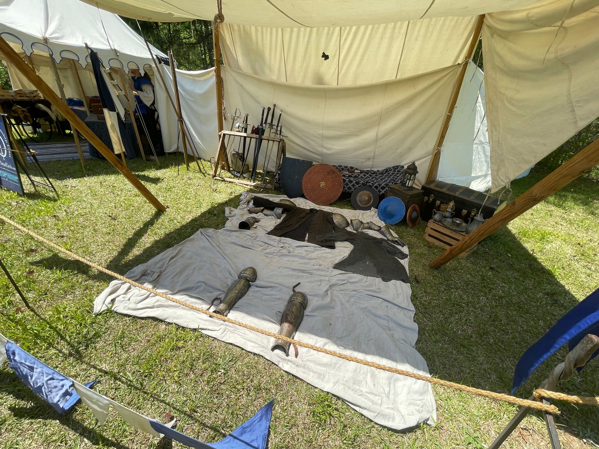 A set of armor laying out on a blanket. Swords and shields are displayed behind.