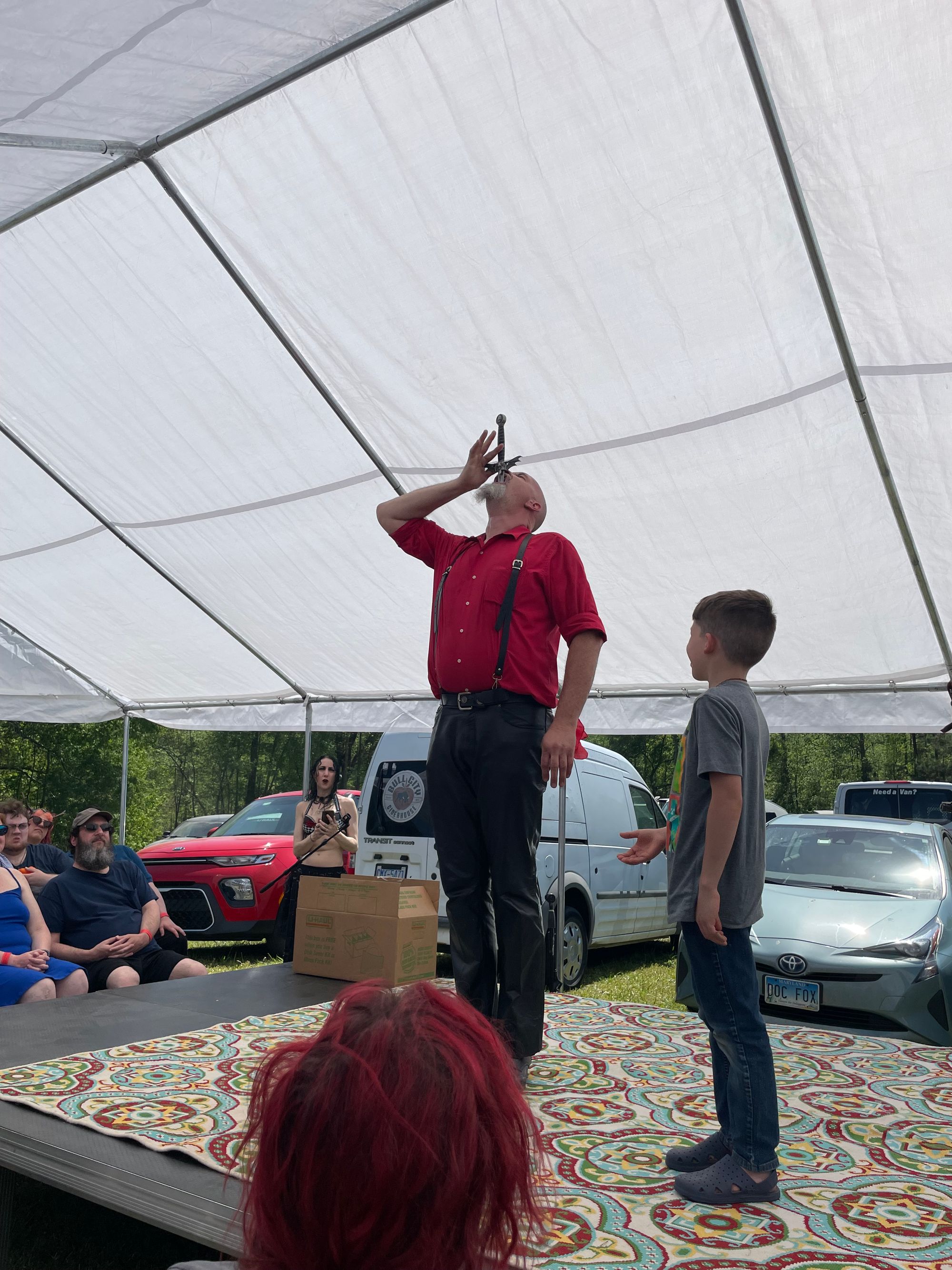 A man swallows a sword while a child is on stage beside him.