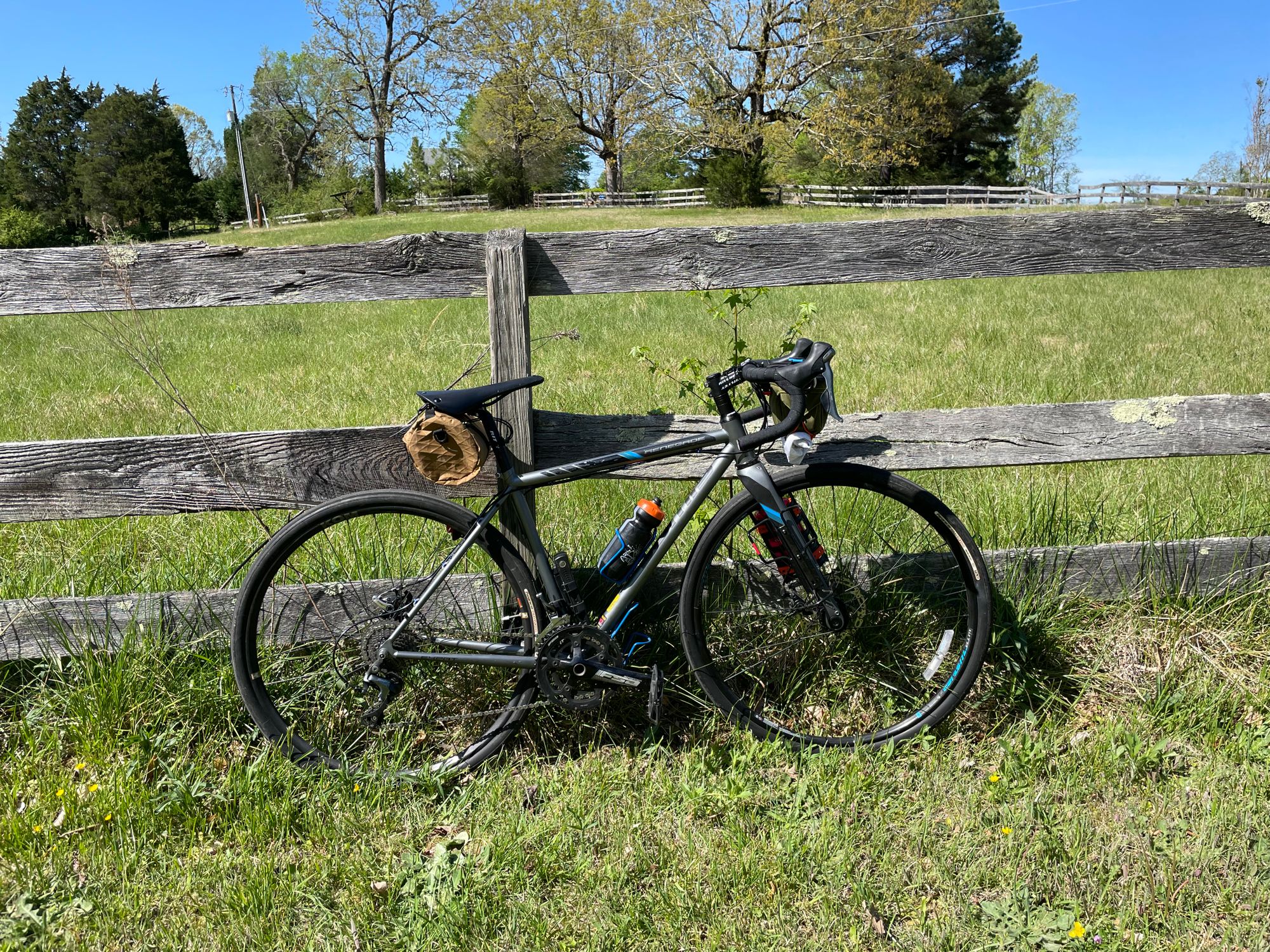 A road bike leans against a wooden fence. It's very green and grassy.