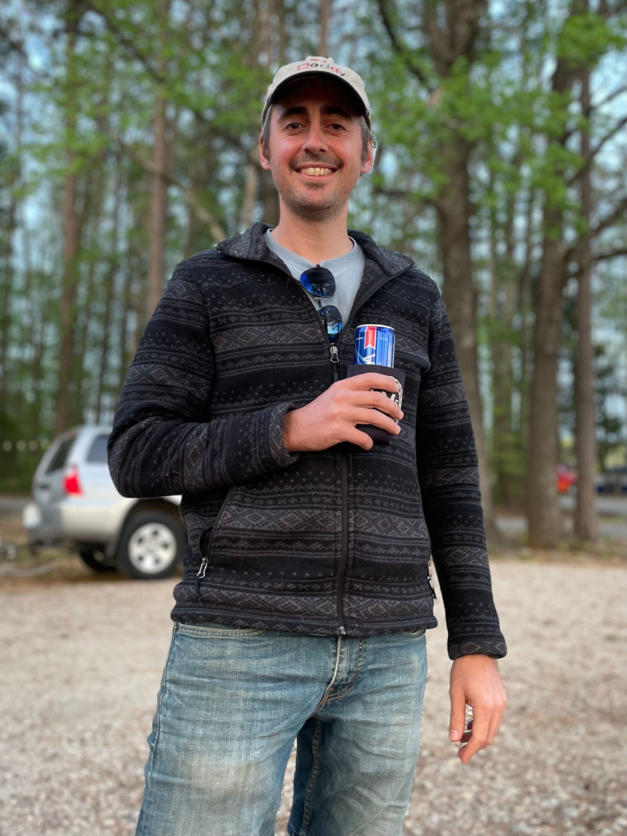 White man holding a can. He's smiling and wearing a cap that says "#1 Daddy."