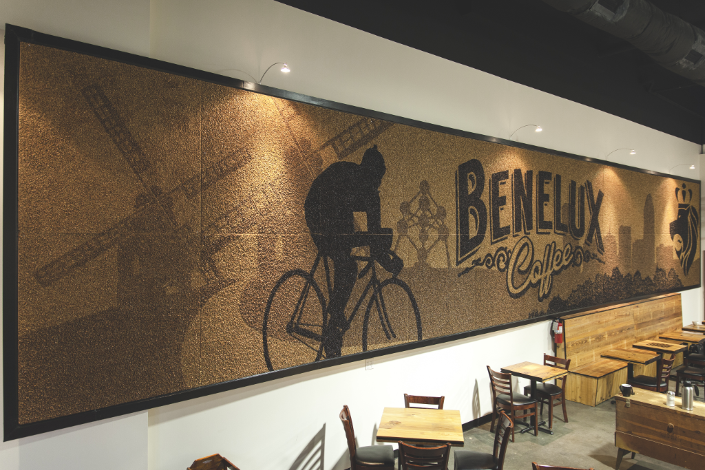 A mural spanning the entire wall made of coffee beans depicts a person on a bicycle. Tables and chairs line the wall below.