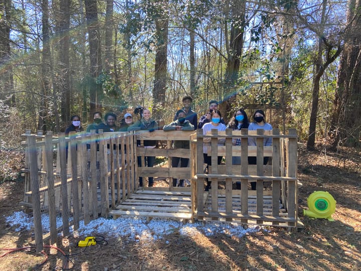 Three compost areas made out of pallets. A group of 11 people stand behind it.