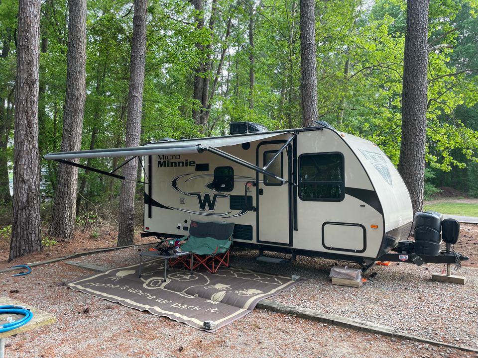 Winnebago travel trailer. There's a double camp chair and table underneath the awning.